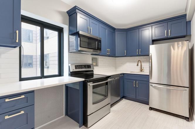 Condo kitchen with navy cabinets, brass pulls and stainless appliances