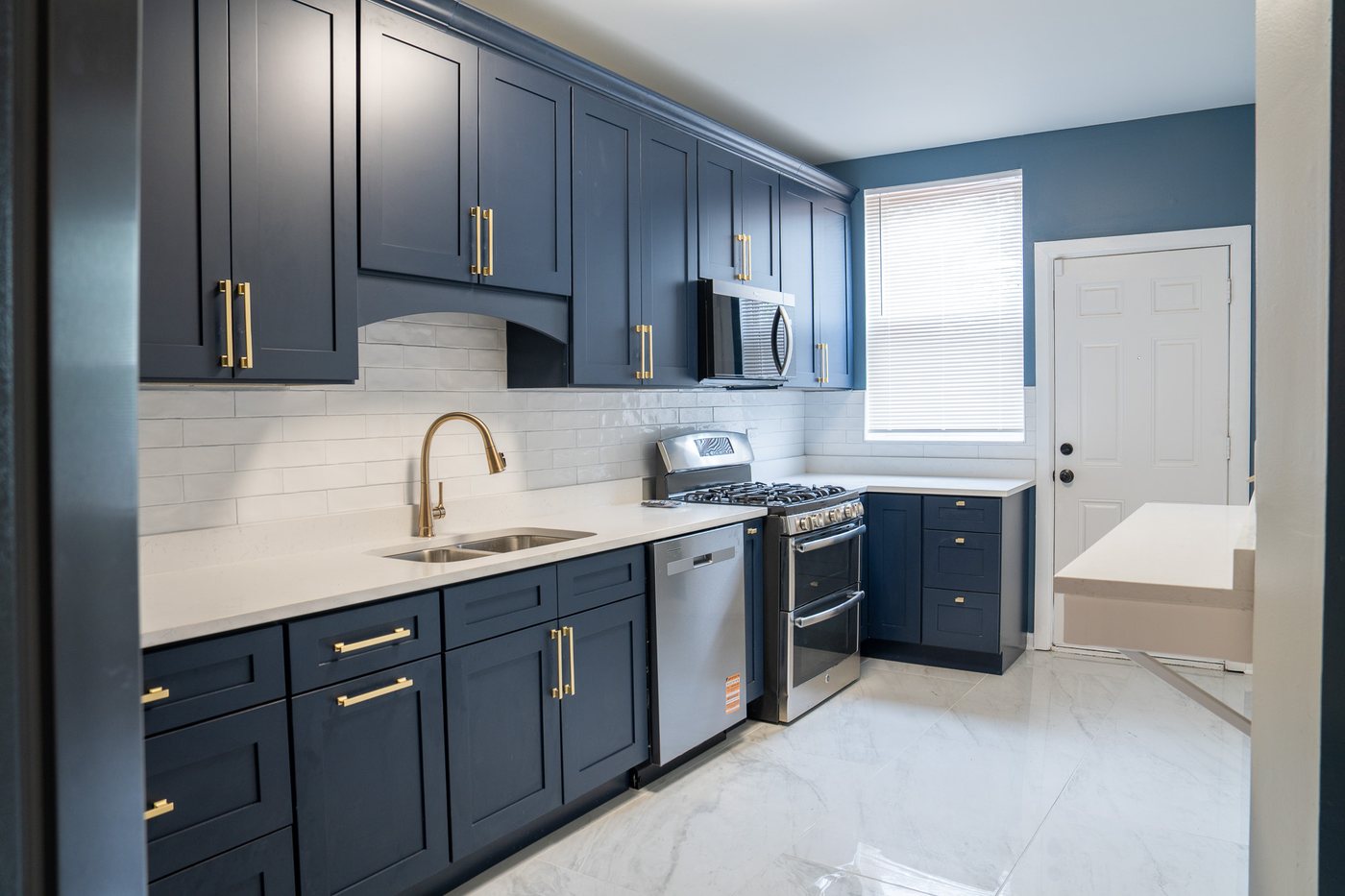 Renovated kitchen with navy cabinets, brass hardware, quartz counters and stainless appliances